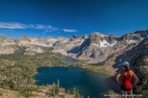 A person standing on top of a mountain near the water.