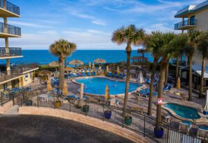 A pool with palm trees and chairs next to the ocean.