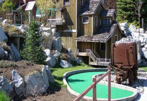 A miniature golf course with a house and train tracks.