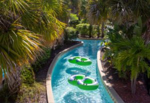 A lazy river with three green tubes going down it.