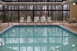 Indoor pool with lounge chairs and trees reflected in water.