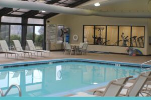 Indoor pool with lounge chairs and gym view.