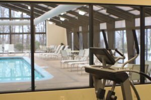 Indoor pool with lounge chairs and an elliptical machine.