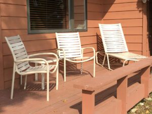 Three white chairs on wooden porch.