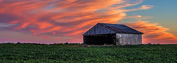 Barn in field at sunset with clouds.