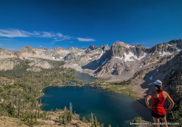 A person standing on top of a mountain near the water.