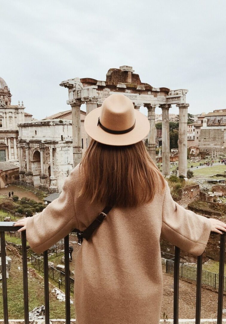 A woman in a hat is looking at the ruins of an old city.